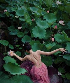 a woman in a pink dress is sitting on some water lilies with her arms outstretched