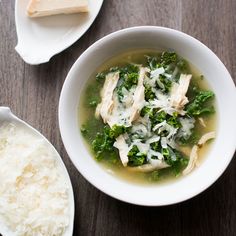 a bowl of chicken and spinach soup next to some rice on a wooden table