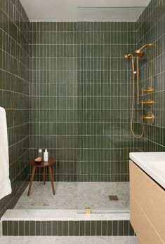 a green tiled bathroom with a wooden stool and shower head in the corner next to it