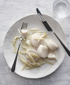 a white plate topped with meat and noodles next to a fork on top of a table