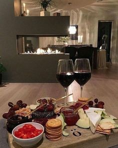 two glasses of wine and some food on a wooden table in front of a fireplace