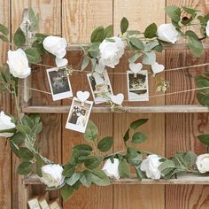 white roses and photos are hanging on a wooden shelf with clothes pins attached to them