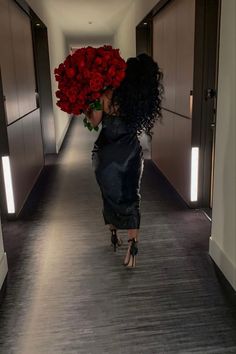 a woman walking down a hallway holding a bunch of red roses