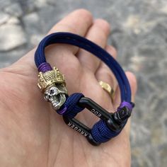 Dual metal bead with garnet stone insert eye, logo shackle on Royal blue cord with purple details. Adjustable Jewelry With Custom Hardware For Gift, Eye Logo, Purple Details, Metal Bead, Garnet Stone, Paracord Bracelets, Metal Beads, Paracord, Handmade Bracelets