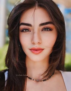 a woman with long brown hair wearing a choker necklace and looking at the camera