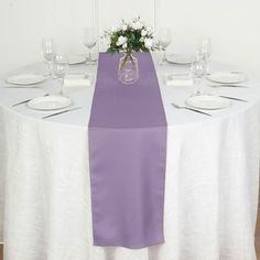 the table is set with white plates and silverware, along with a purple runner