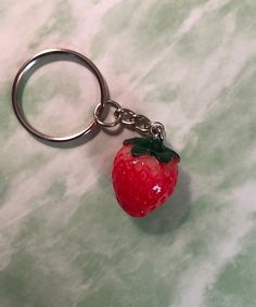 a red strawberry keychain with a black leaf on it's end sitting on a marble surface