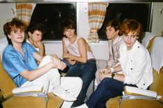 four young men sitting on seats in a train, one with his arm around the other's neck