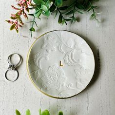 a wedding ring sits on top of a white plate next to flowers and a pair of scissors