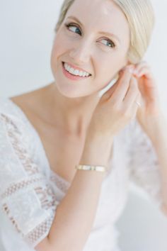 a woman is smiling and talking on her cell phone while wearing a white dress with lacy sleeves