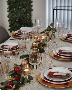 the table is set for christmas dinner with candles and greenery on each place setting