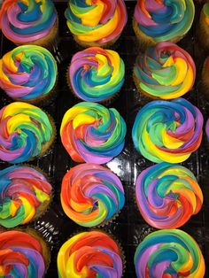 cupcakes with multi colored frosting on top of each other in plastic wrappers