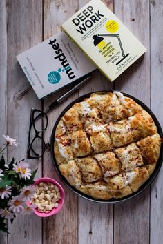 a pizza sitting on top of a wooden table next to a book and some flowers