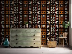 an old dresser in front of a wallpaper with geometric designs on it and a basket next to it