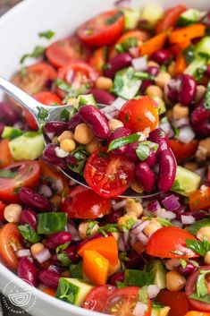 a salad with beans, tomatoes, cucumbers and other vegetables is being held by a spoon