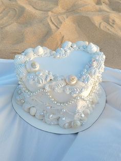 a white wedding cake with pearls and seashells on the top is sitting in the sand