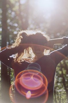 a woman holding a frisbee in front of her face with the sun shining behind her