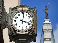 a clock on the side of a building with a statue in the background