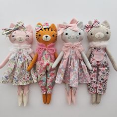 four stuffed animals are lined up on a white surface and one is wearing a pink dress