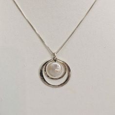 "This elegant pendant is made of sterling silver and features an 10- 12 mm round coin shaped pearl. The clean simple design of this pendant is 1\" wide with two hammered circles of silver. This piece could be a perfect complement to a wedding dress. Please choose whether you would like a white pearl or a peacock pearl. The pendant comes on a .85 mm wide box link chain with a lobster claw. Please select what length chain you would prefer. If you choose the 24\" chain, it is 1 mm wide and has a sp Circular Pearl Pendant Jewelry Gift, Pearl Necklace With Coin Pendant As Gift, Everyday Pearl Necklace With Round Pearl Pendant, Sterling Silver Round Jewelry With Pearl Charm, Nickel-free Round Pearl Jewelry, Everyday Pearl Necklace With Pearl Pendant, Nickel-free Pearl Jewelry, Silver Round Pearl Drop Jewelry, Everyday Pearl Necklace With Round Pendant