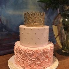 a three tiered cake decorated with pink roses and a gold crown on the top