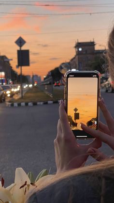 a woman is taking a photo with her cell phone at the street corner as the sun sets