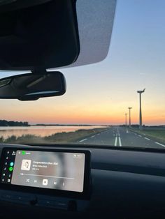 the dashboard of a car on a highway with windmills in the background at sunset