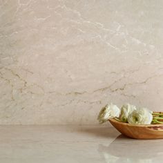 white flowers in a wooden bowl on a marble countertop next to a beige wall