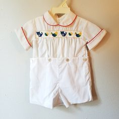 "- This classic vintage outfit by C.I. Castro and Co. is perfect for a party! This all white outfit is 2 pieces with simple button on shorts. The shirt is gathered at the front and has a retro ribbon trim across chest that features a blue cat, bird, and beach ball. The peter pan collar and cuffs are piped in red. Shirt buttons down back. Shorts snap between legs. Size is: 12 months Length: 15\" + 4\" where buttons on waist can be lowered" Classic White Sets For Summer, Fitted Vintage White Sets, Retro White Short Sleeve Shirt With Camp Collar, Vintage White Sets For Summer, White Vintage Cotton Sets, Vintage Collared Beach Tops, Vintage White Summer Sets, White 2 Piece Outfit, White Fitted Playwear Set