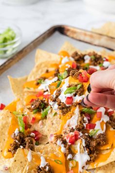 a person is holding a tortilla chip in front of some nachos