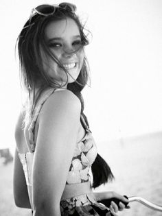 a black and white photo of a woman on the beach with her hair blowing in the wind