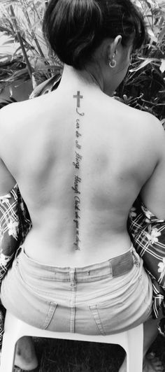 a woman with a cross tattoo on her back is sitting in front of some plants