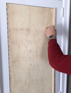 a person is holding up a piece of plywood board to the door with their hand