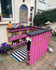 an outdoor bar made out of pallet wood with pink paint and black counter tops