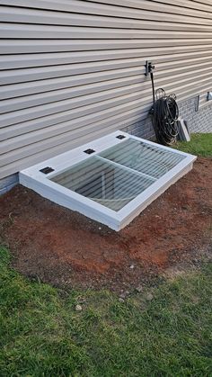 a white box sitting on top of a grass covered field next to a building with a hose attached to it