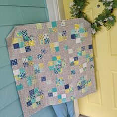 a person holding up a quilt in front of a yellow door with blue and white flowers