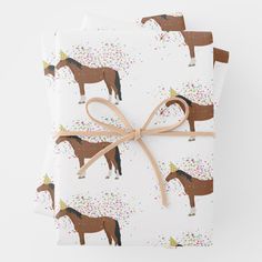 wrapping paper with horses and confetti on it, tied in a brown ribbon