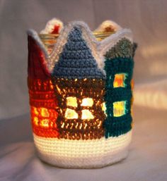 a crocheted cup with a lit up house in the middle and two windows on each side