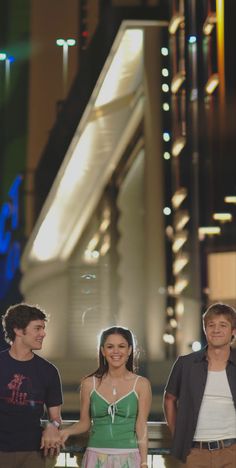 three young people standing next to each other in front of a building at night time