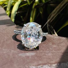 an oval diamond ring sitting on top of a stone slab in front of some plants