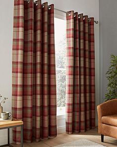 a living room filled with furniture and a window covered in red plaid drapes next to a brown chair