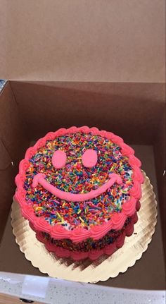 a birthday cake with sprinkles and a smiley face on it in a box