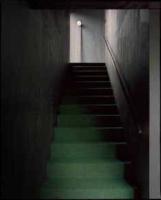 green carpeted stairs leading up to a light on the wall in a dark room