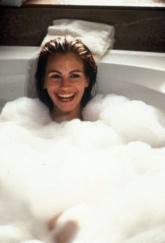 a woman smiles as she takes a bubble bath