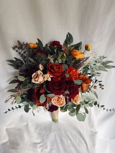 a bridal bouquet with orange and red flowers on a white cloth background in the studio