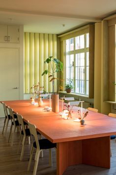 a long wooden table with plants in vases and candles on it next to a window