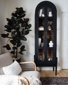 a living room with a black china cabinet next to a white chair and potted plant