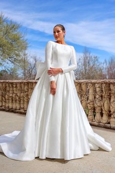 a woman in a white wedding dress standing on a bridge with her hands on her hips