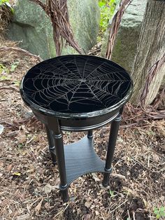 a spider web table sitting on the ground in front of a tree and some rocks