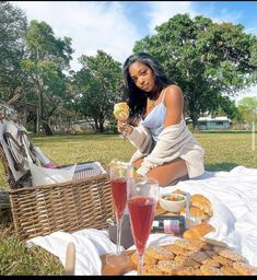 a woman sitting on a blanket with food and drinks